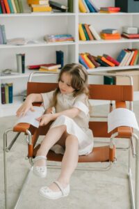 A young girl sitting in a modern library surrounded by colorful books, engrossed in reading.