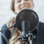 A woman smiles while recording with a professional microphone. Perfect for media and broadcasting themes.